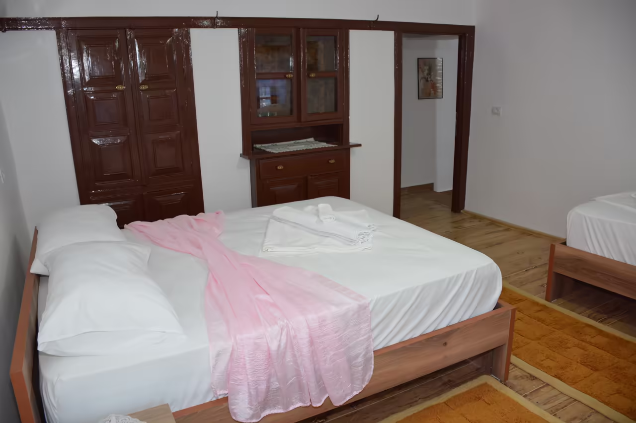 Bedroom with a double bed with a pink throw, a single bed and a wooden wardrobe