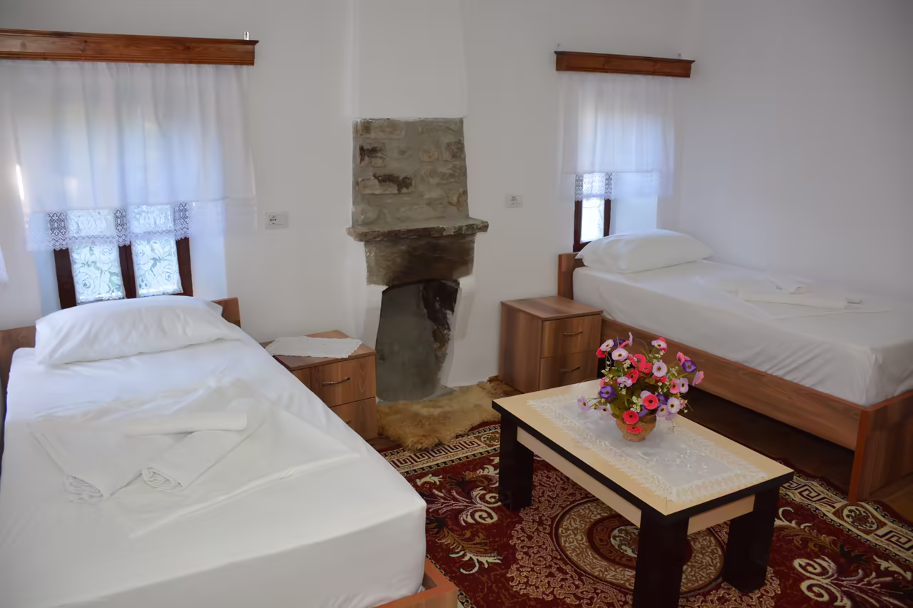 Room with two single beds, a stone fireplace and a coffee table with flowers