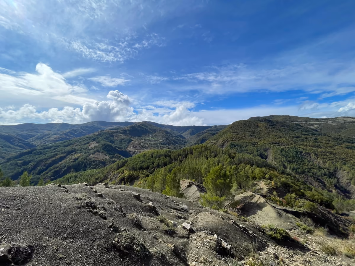 Forested ridges and mountains seen from a bare, rocky slope on the trail