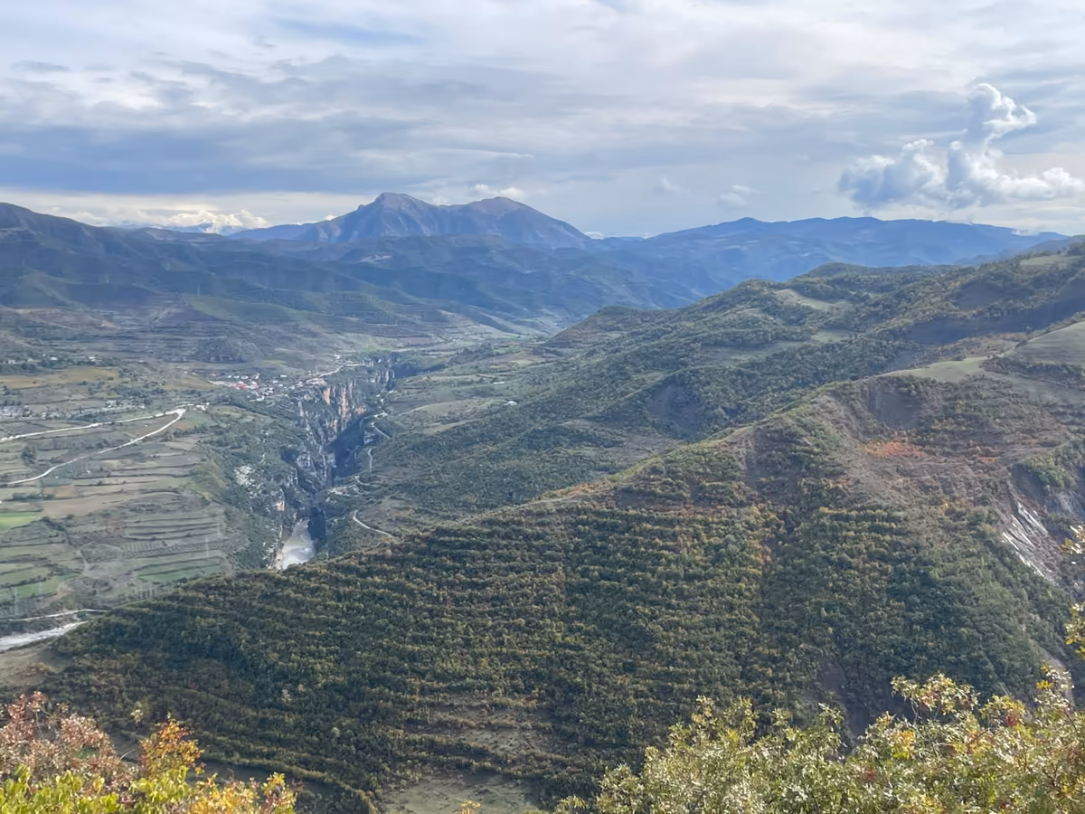 View from the trail down to a river valley, with layered mountains and a peak behind