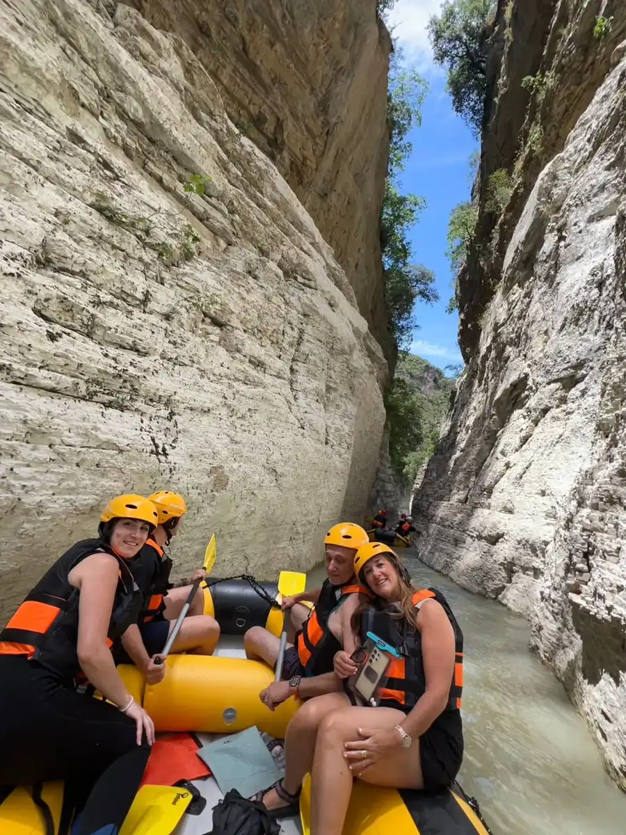 Four rafters in orange helmets smiling between the towering white walls of Osum Canyon