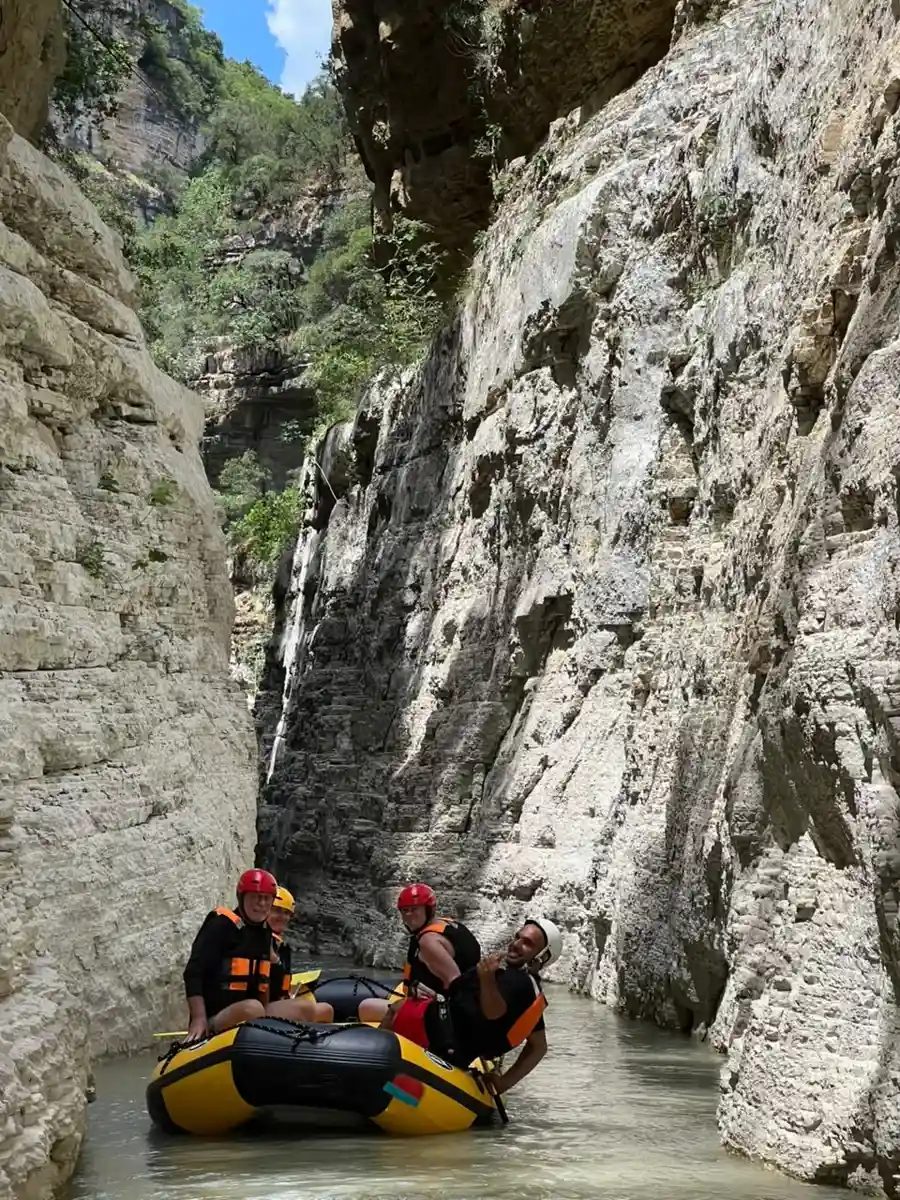 Rafting group beneath a towering striated limestone wall in Osum Canyon