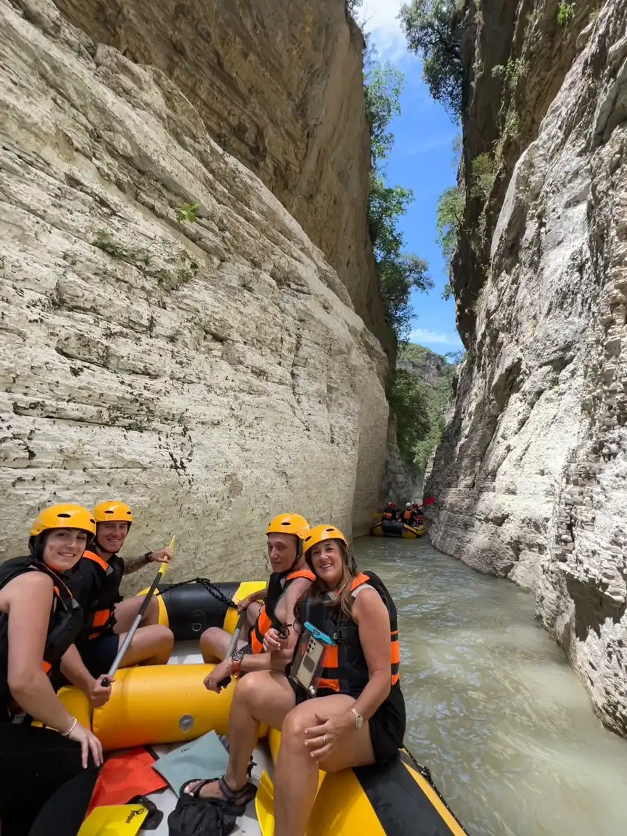 Rafting group in orange helmets, one pointing up at the sheer canyon walls