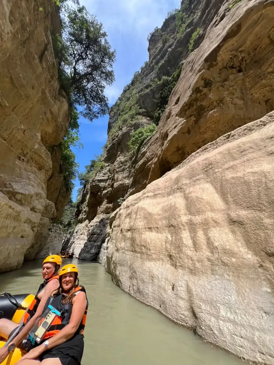 Four rafters with paddles raised on open river below a green forested cliff