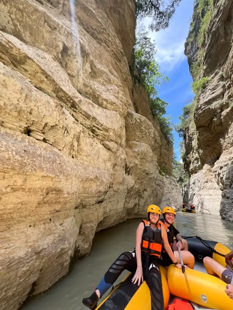 Couple in orange helmets on a raft beneath golden Osum Canyon cliffs