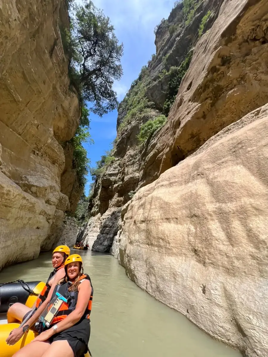 Couple in yellow helmets on a raft beside sandy canyon walls and an overhanging tree