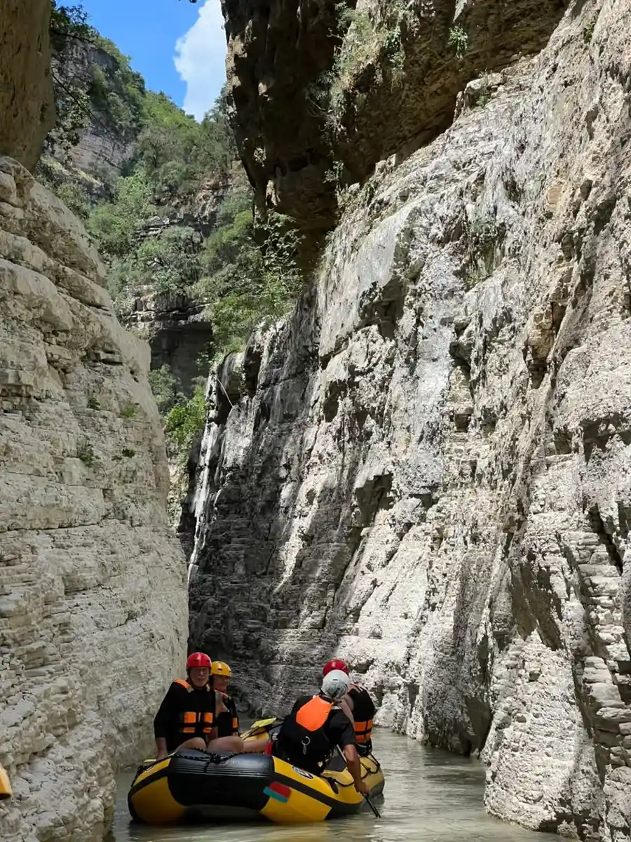 Four rafters in orange helmets with a red paddle, another raft ahead