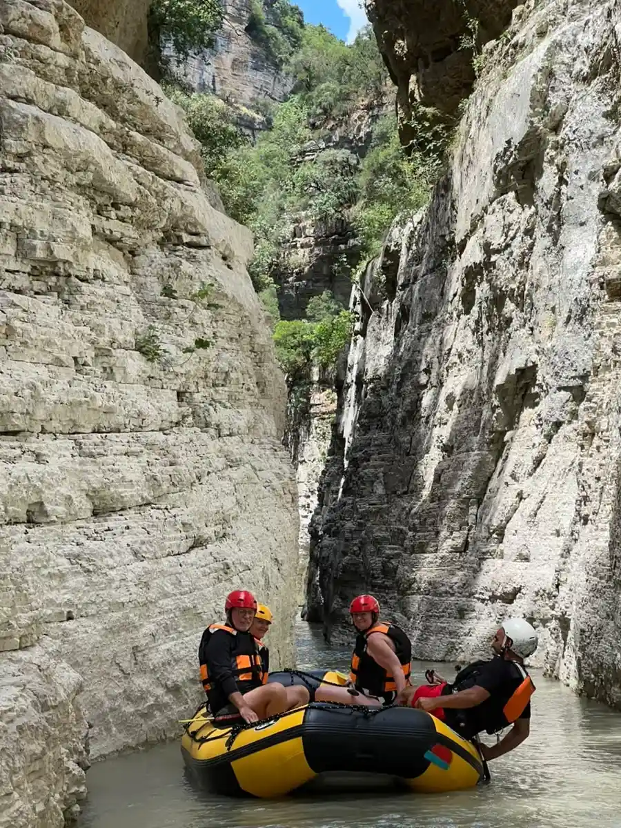 Rafters in red helmets mid-river beneath the high cliffs of Osum Canyon