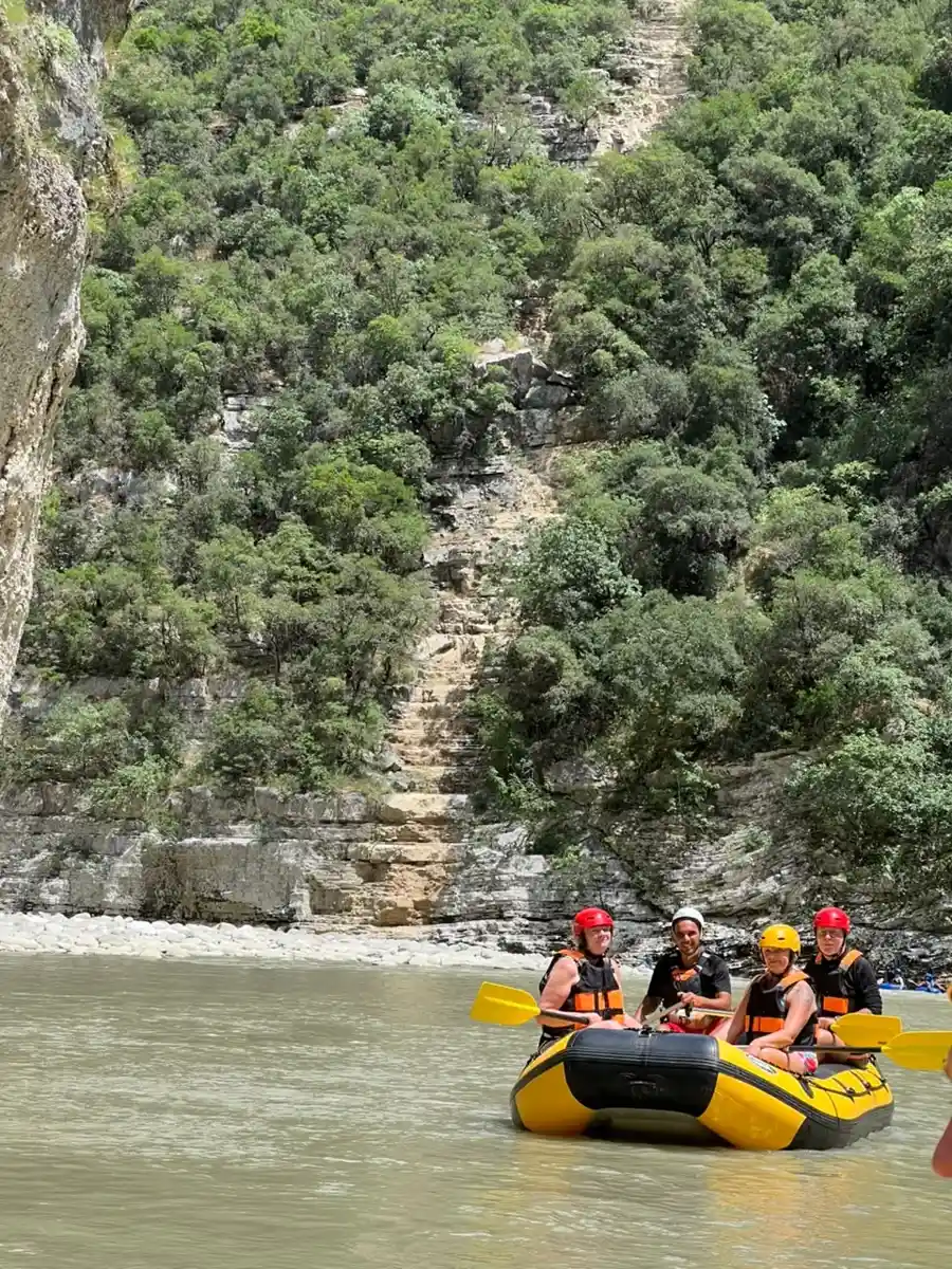 Two rafters in yellow helmets below tan canyon walls with a tree overhead