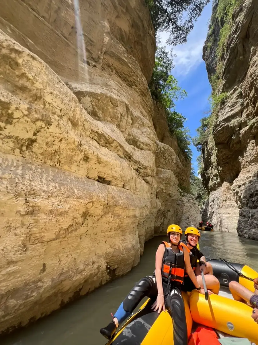 Two smiling rafters under towering golden canyon walls and blue sky