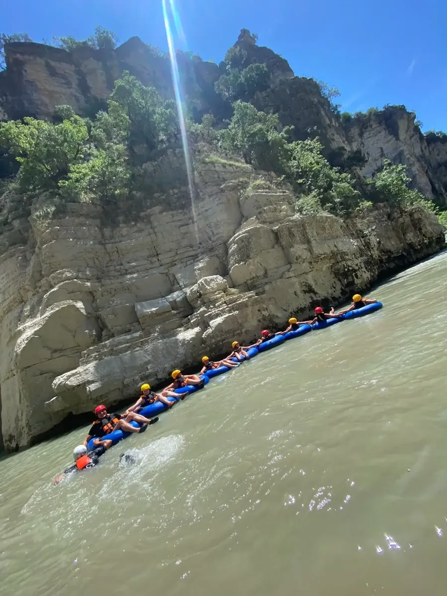 Tubers floating in a line beneath tall canyon cliffs with a guide alongside